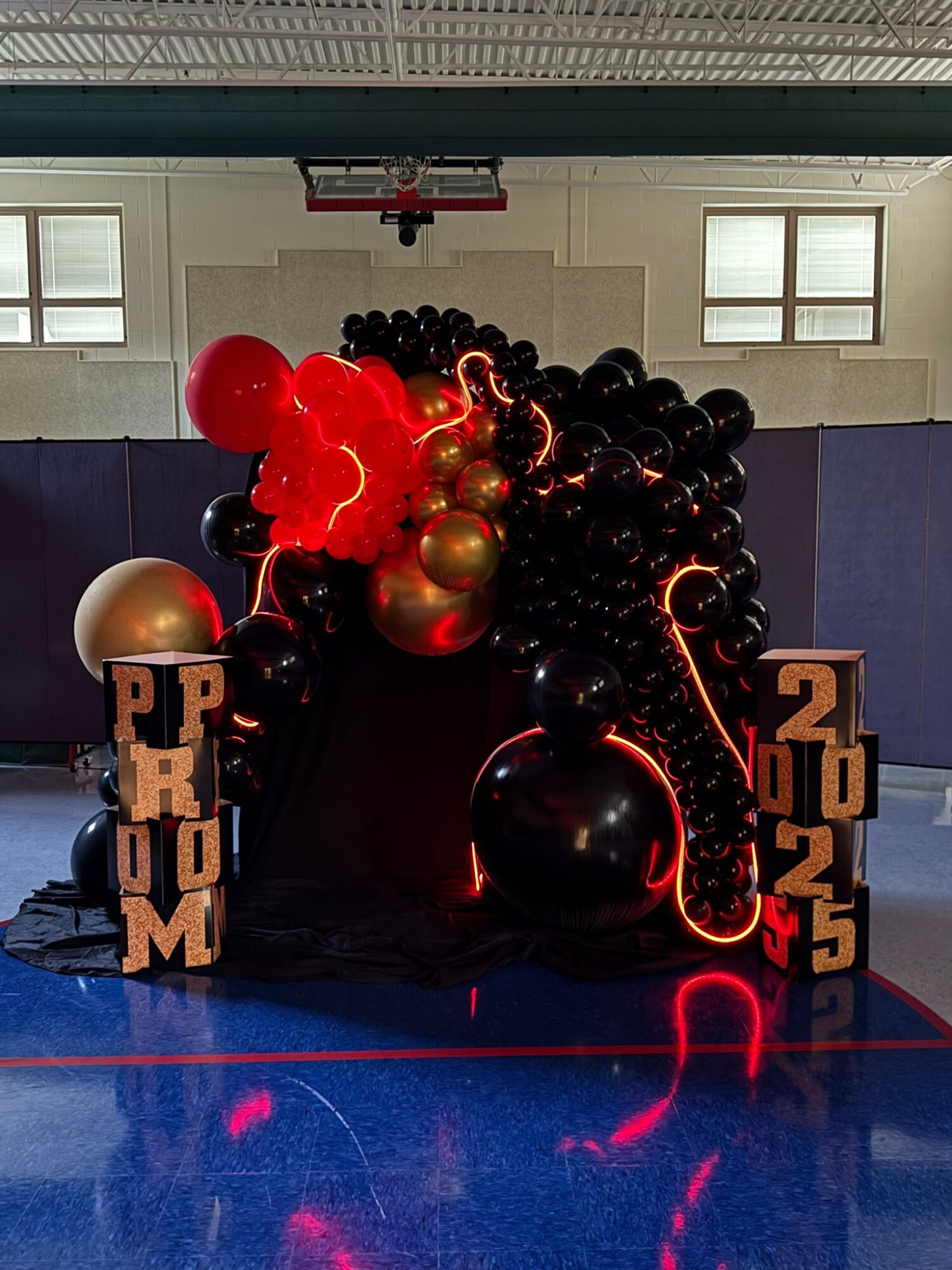 Decorative balloon arrangement with black, red, and gold balloons, and illuminated elements, celebrating a graduation or achievement, with the year 2025.