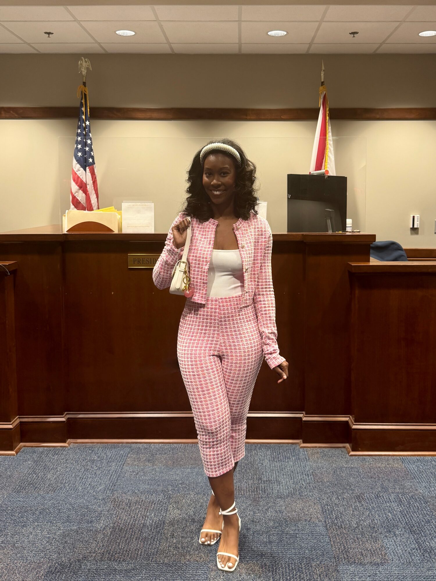 Woman in pink checkered suit standing in a courtroom with American flags behind her.