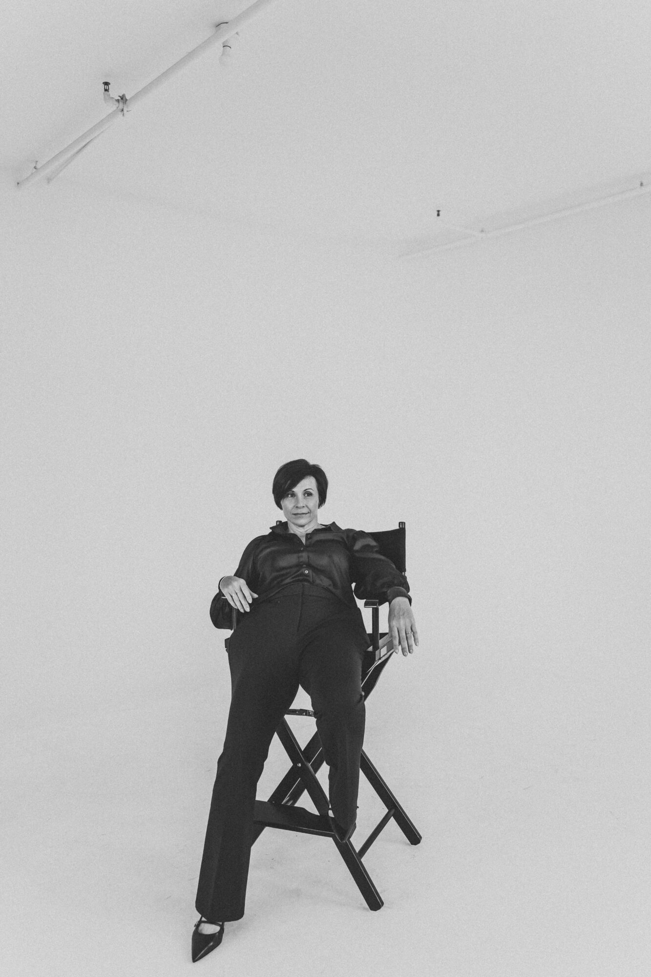 Person standing on a chair in a plain room, holding a camera, with a high ceiling and minimal decor.