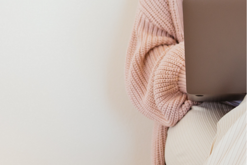 Person wearing a pink sweater holding a laptop, with part of their body visible.