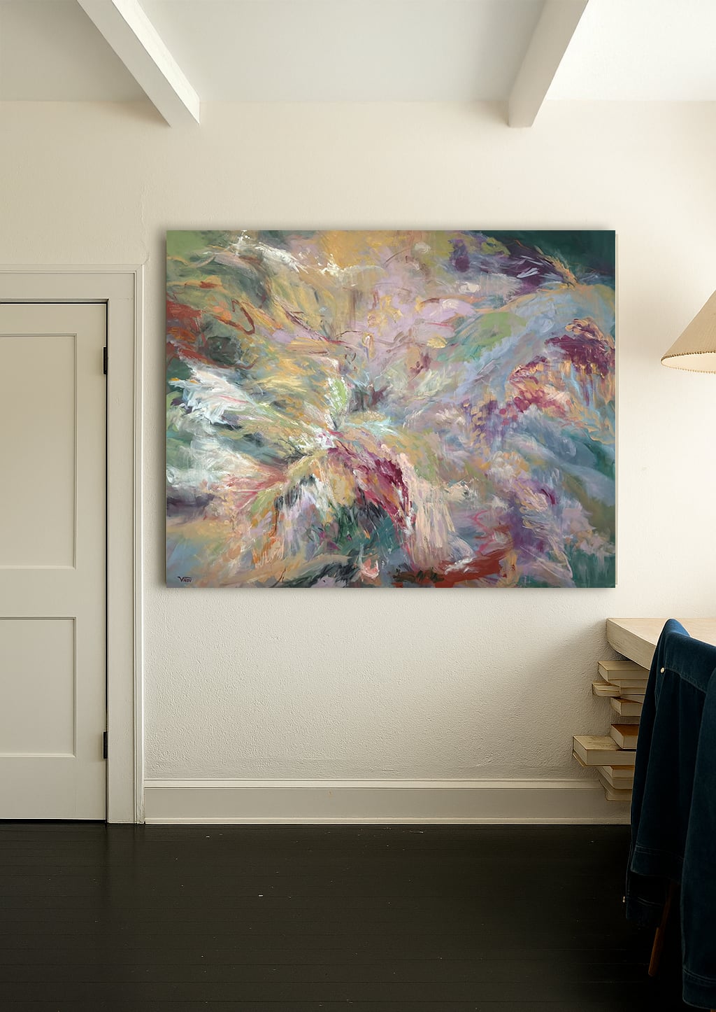 Abstract colorful painting on a white wall in a room with a door and a stack of books.