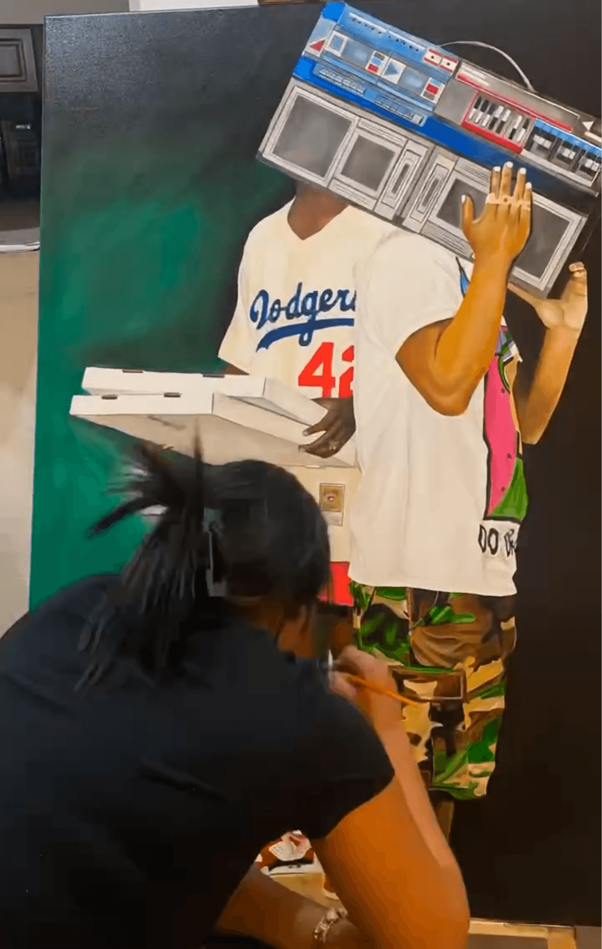 Person with a boombox head and a Dodgers jersey, holding a boombox, with another person sitting nearby, in an indoor setting.