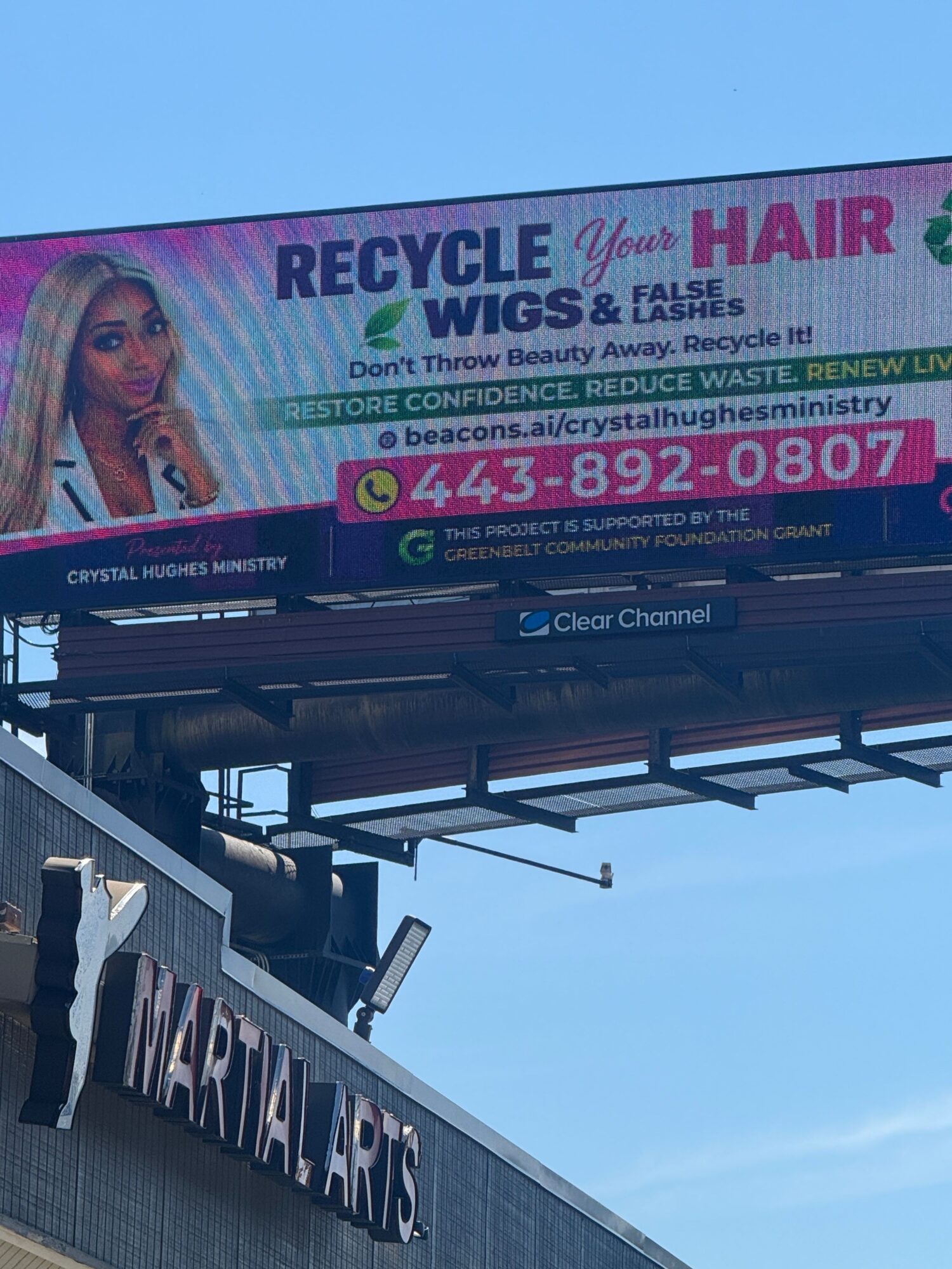 Billboard advertising recycling and hair services, with a woman and contact information, viewed from below against a blue sky.