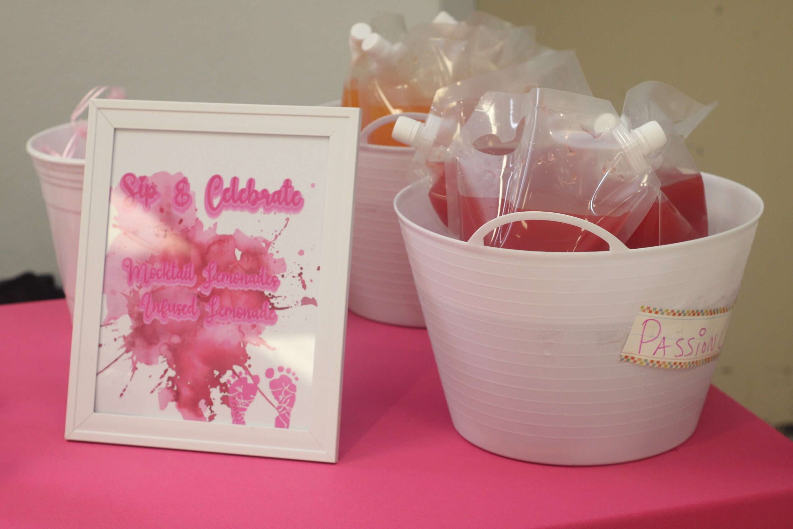 A framed pink and red watercolor art piece next to a white bowl filled with red and clear plastic bags, on a pink surface.