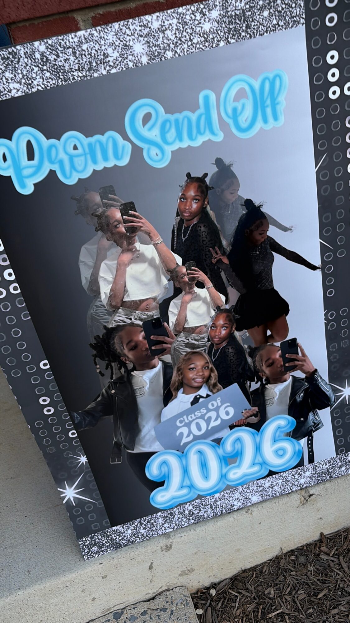 Group of young women taking a selfie in front of a prom send-off sign with the year 2026, smiling and posing.