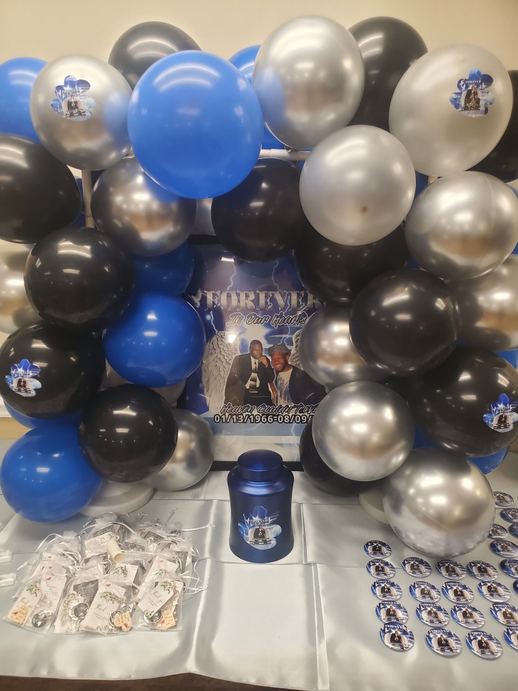 Balloon display with black, silver, and blue balloons, a poster, and a table with party favors.