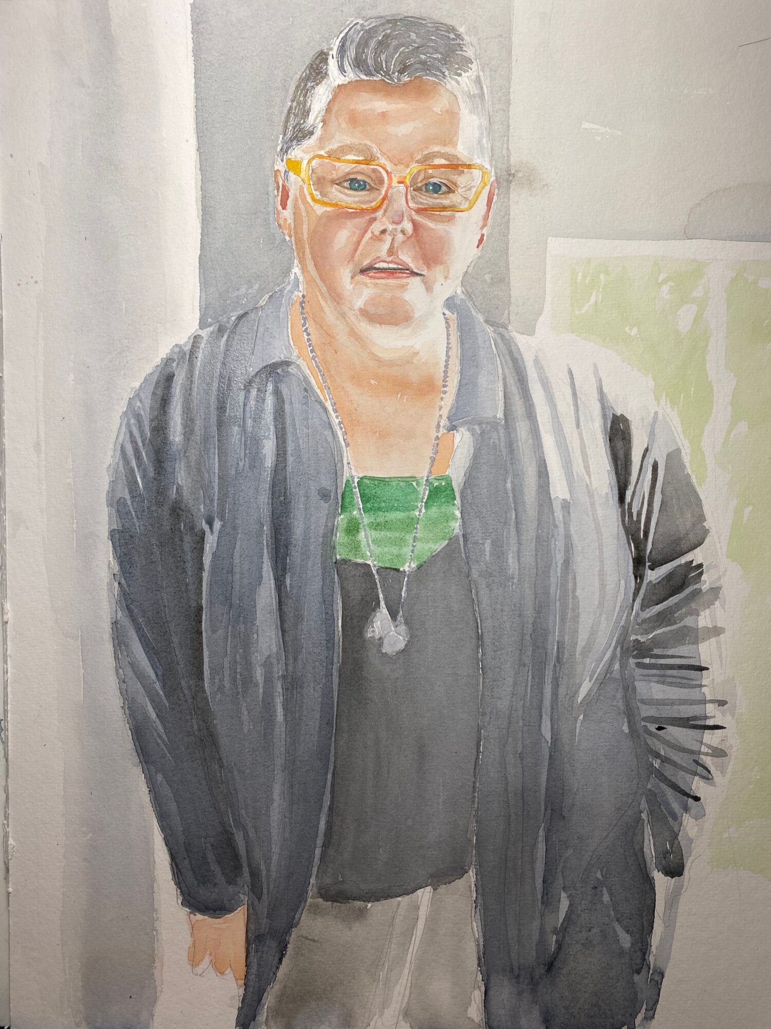 Portrait of a woman with glasses, wearing a dark jacket and a green top, smiling, with a painting in the background.