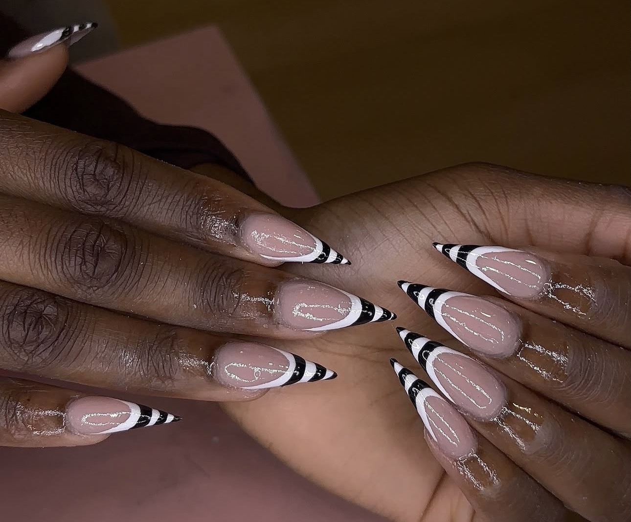 Two hands with manicured nails featuring black and white striped tips and clear polish, resting on a pink surface.