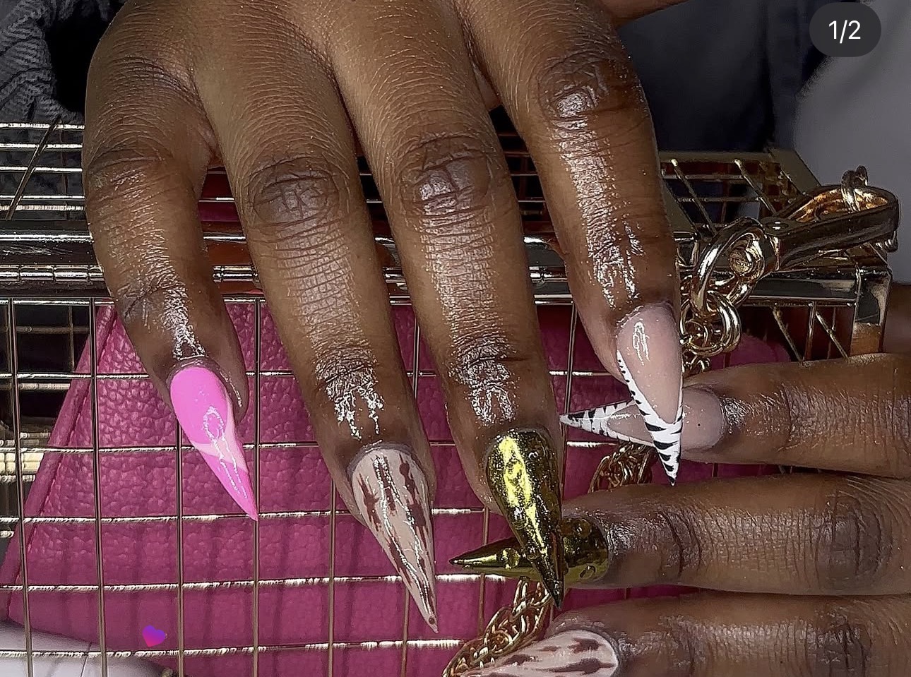 Close-up of hands with long, decorated nails resting on a wire surface, with a pink cloth underneath, and a keychain in hand.