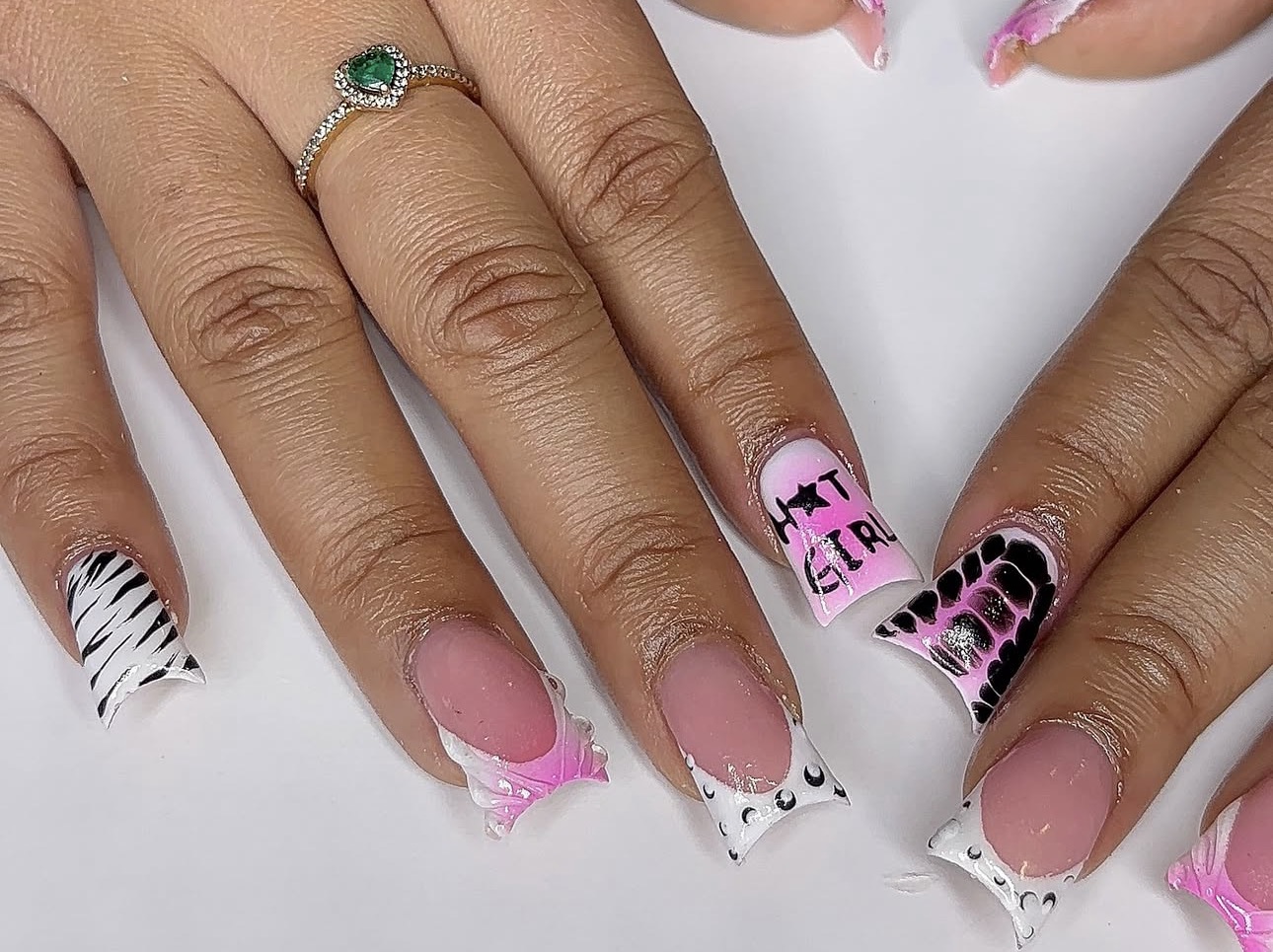 Close-up of hands with decorated nails, one hand has a ring with a green stone, nails with pink, black, and white designs.