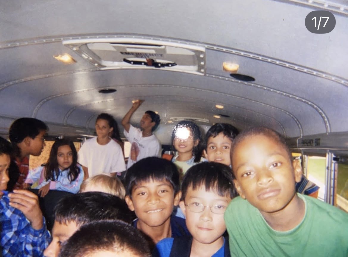 Group of children inside a bus, some smiling and looking at the camera, with a curved ceiling overhead.