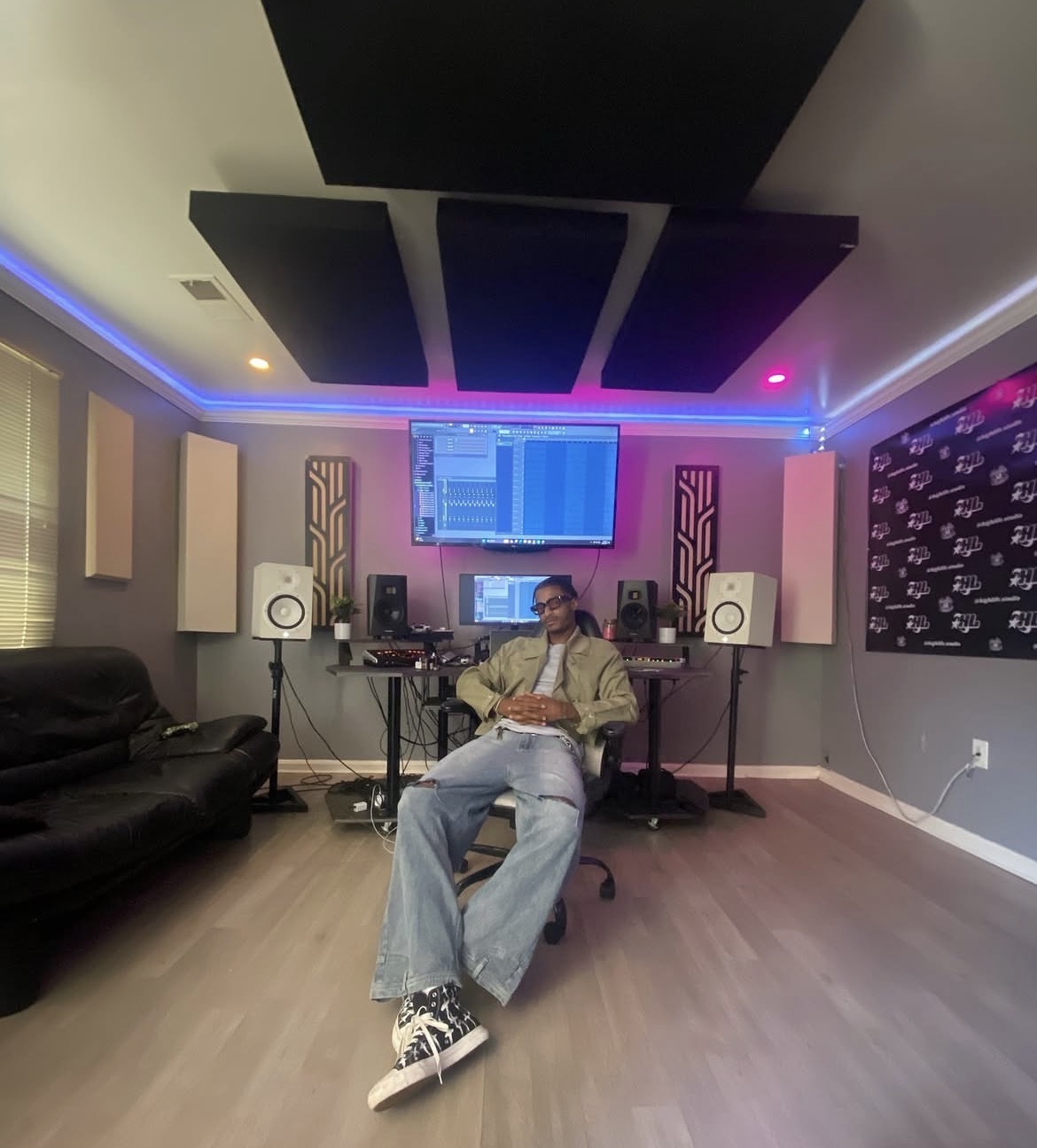 Person sitting in a music studio with equipment, speakers, and soundproofing panels on the walls.