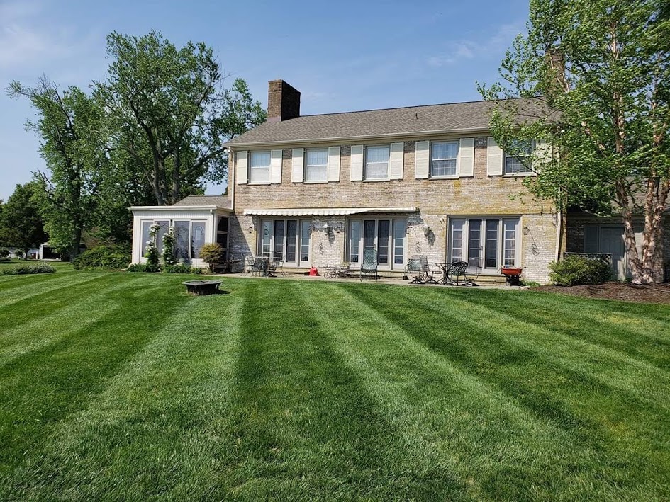 Large house with a well-maintained lawn, trees, and a clear blue sky.