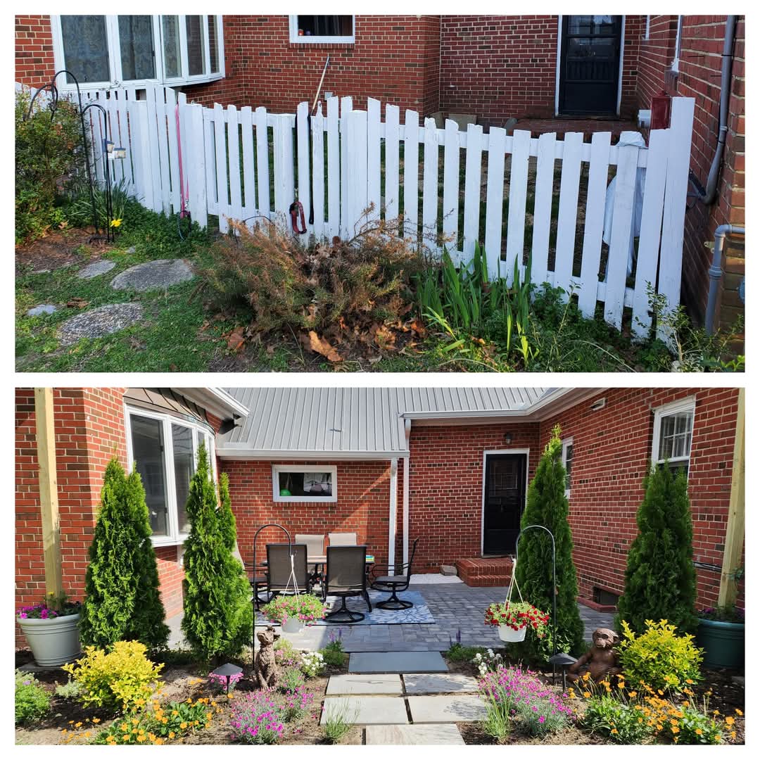 Backyard with white picket fence, garden, patio, and potted plants, brick house in background.