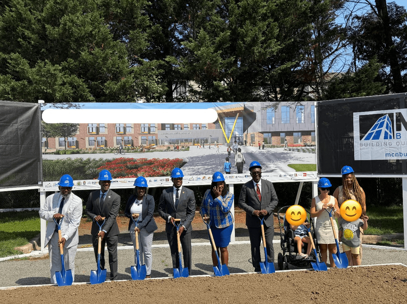 Group of people at a groundbreaking ceremony, some holding shovels, with a banner and trees in the background.