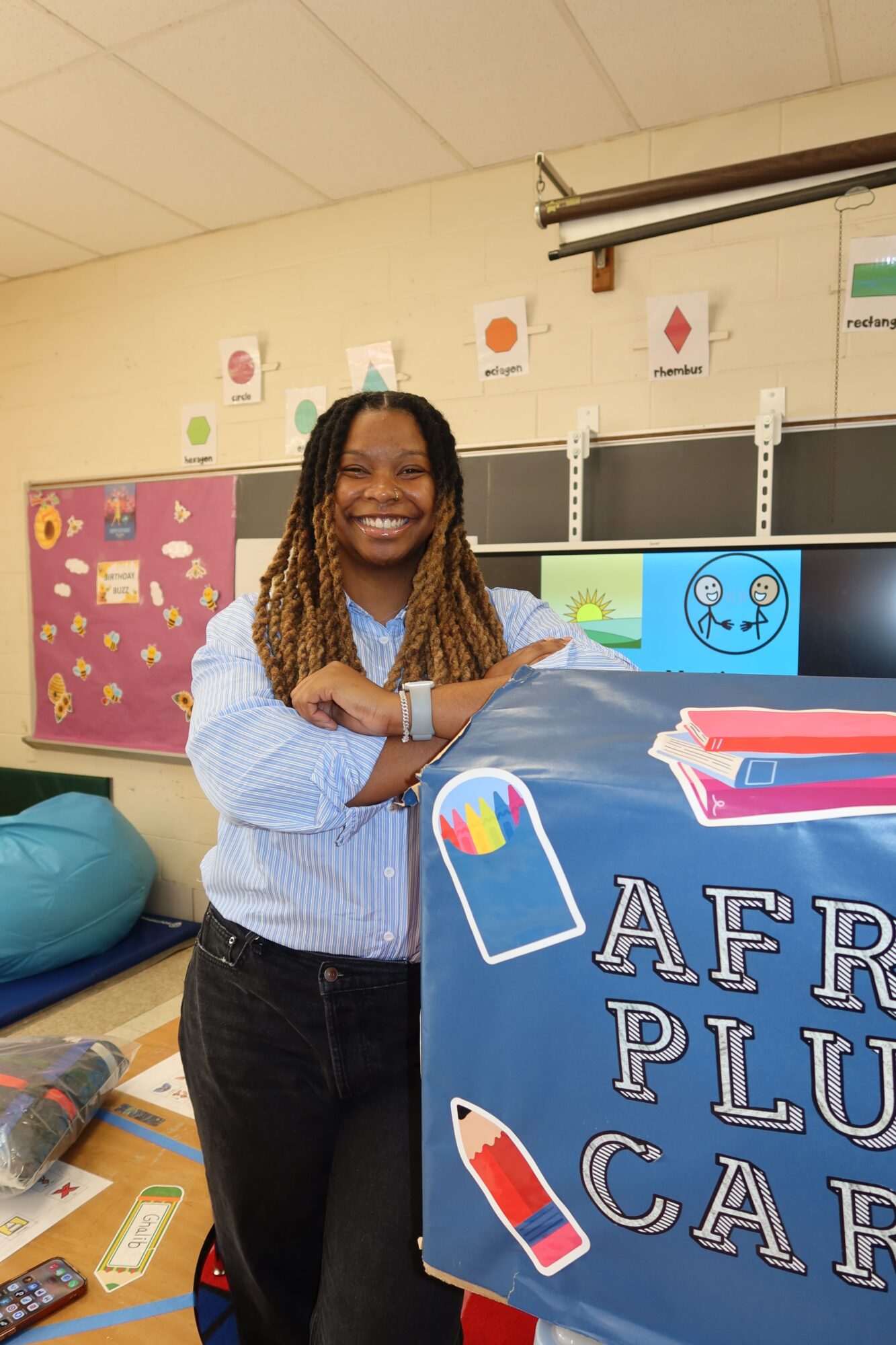 Woman standing behind a table with a sign that reads 'AFRICA PLU' in a classroom.