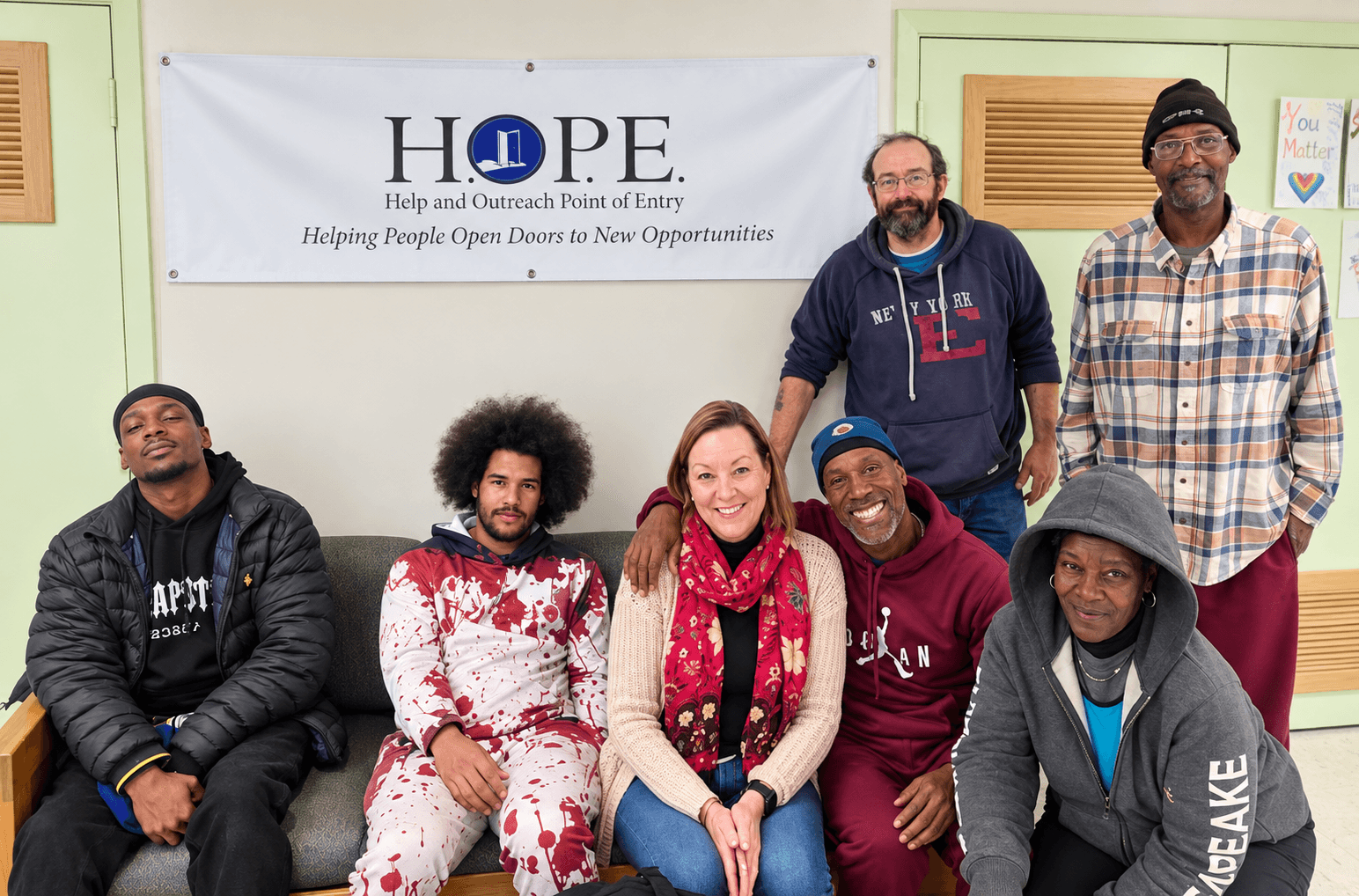 Group of seven diverse people smiling in a room with a Hope banner on the wall.