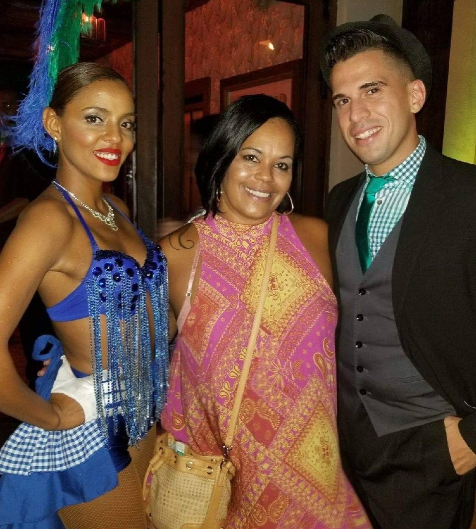 Three people smiling at a party, two women and one man, dressed in colorful outfits, standing indoors.