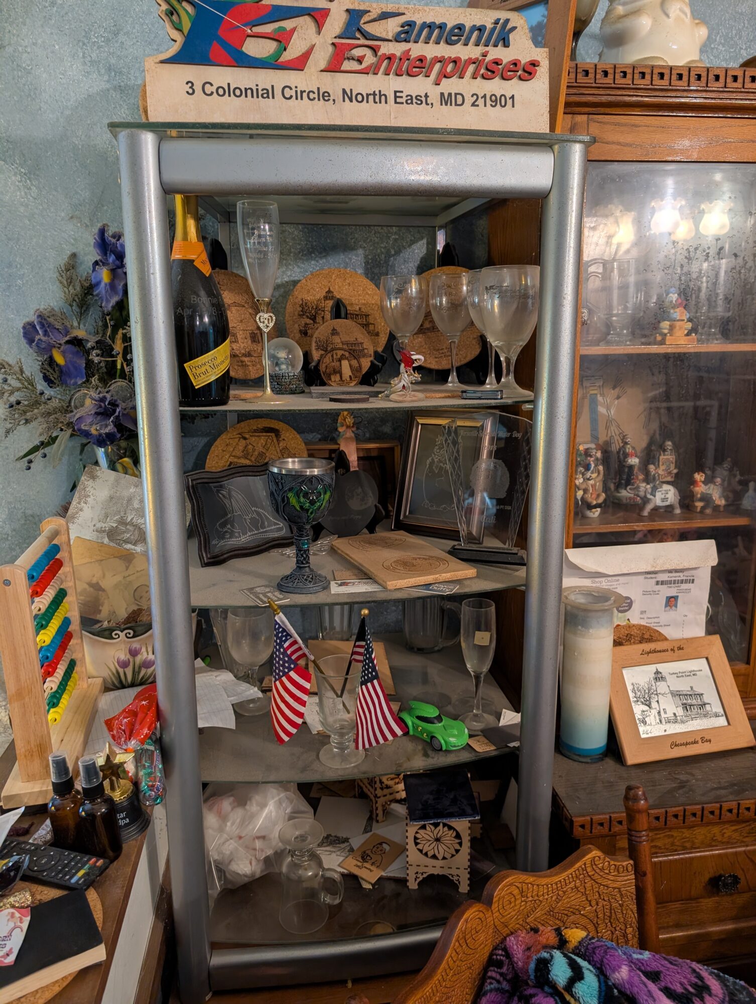 Glass display case filled with decorative items, flags, and glassware, surrounded by various objects and furniture in a room.