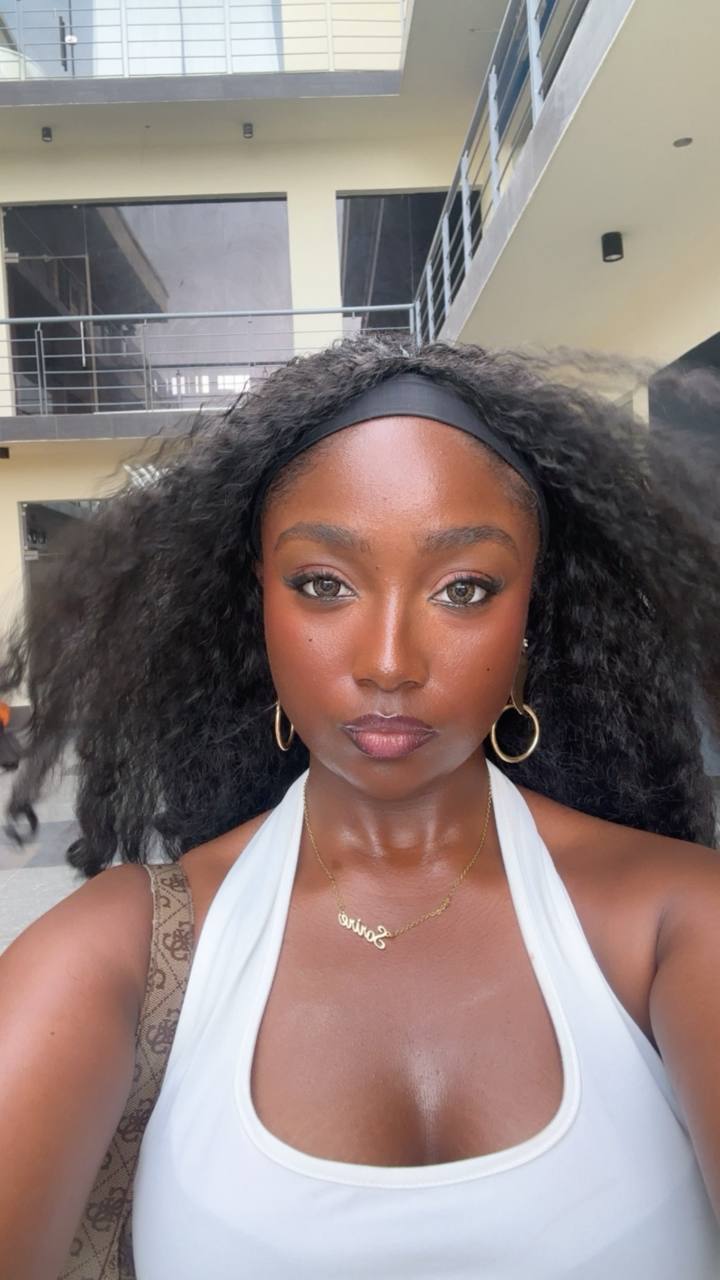 Young woman with curly hair taking a selfie indoors, wearing a white top and hoop earrings.