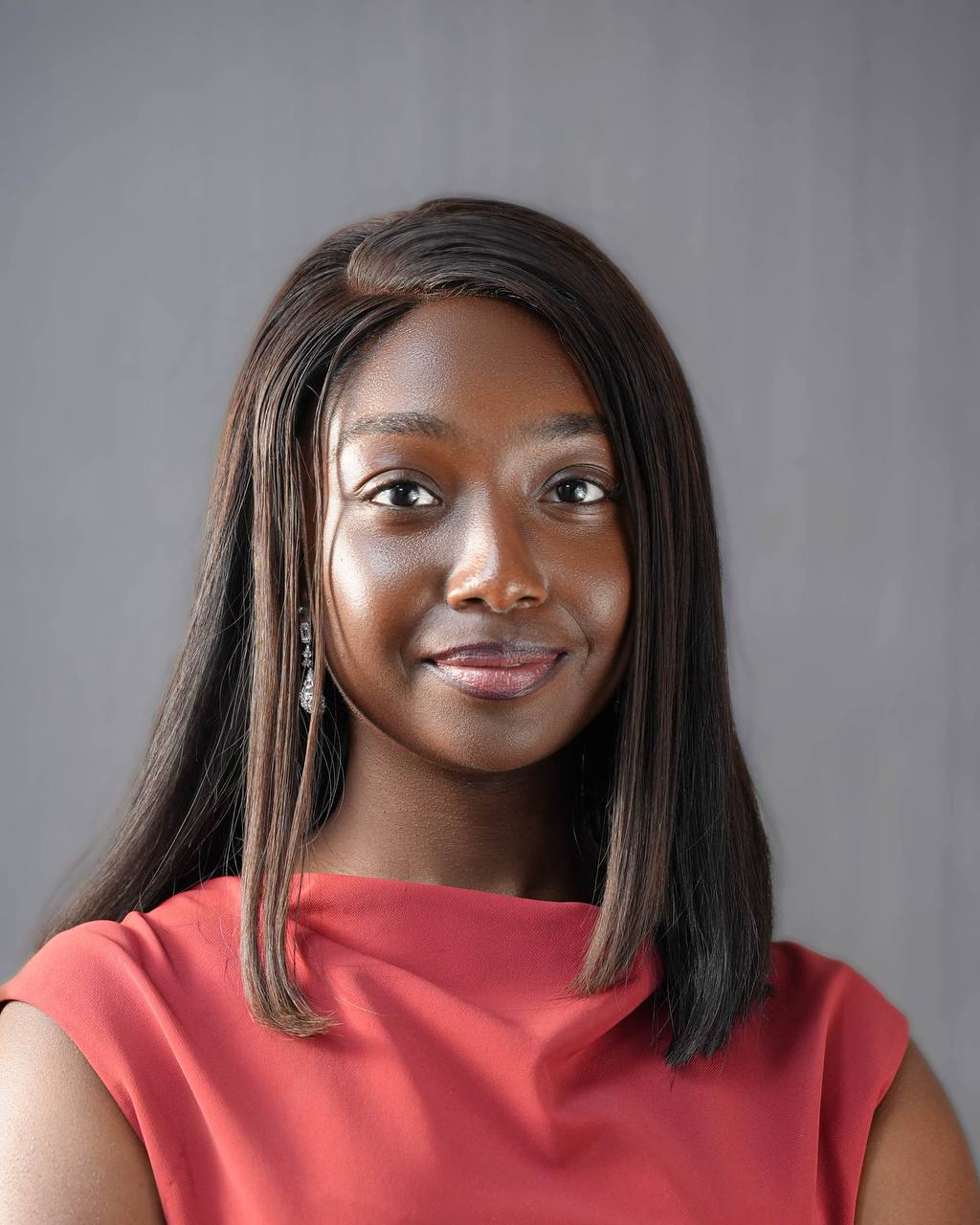 Young woman with straight, shoulder-length hair, wearing a red top, smiling softly against a gray background.