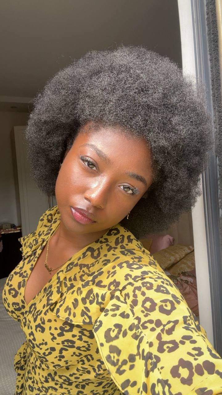 Woman with natural afro hairstyle wearing a yellow leopard print top, looking at the camera indoors.
