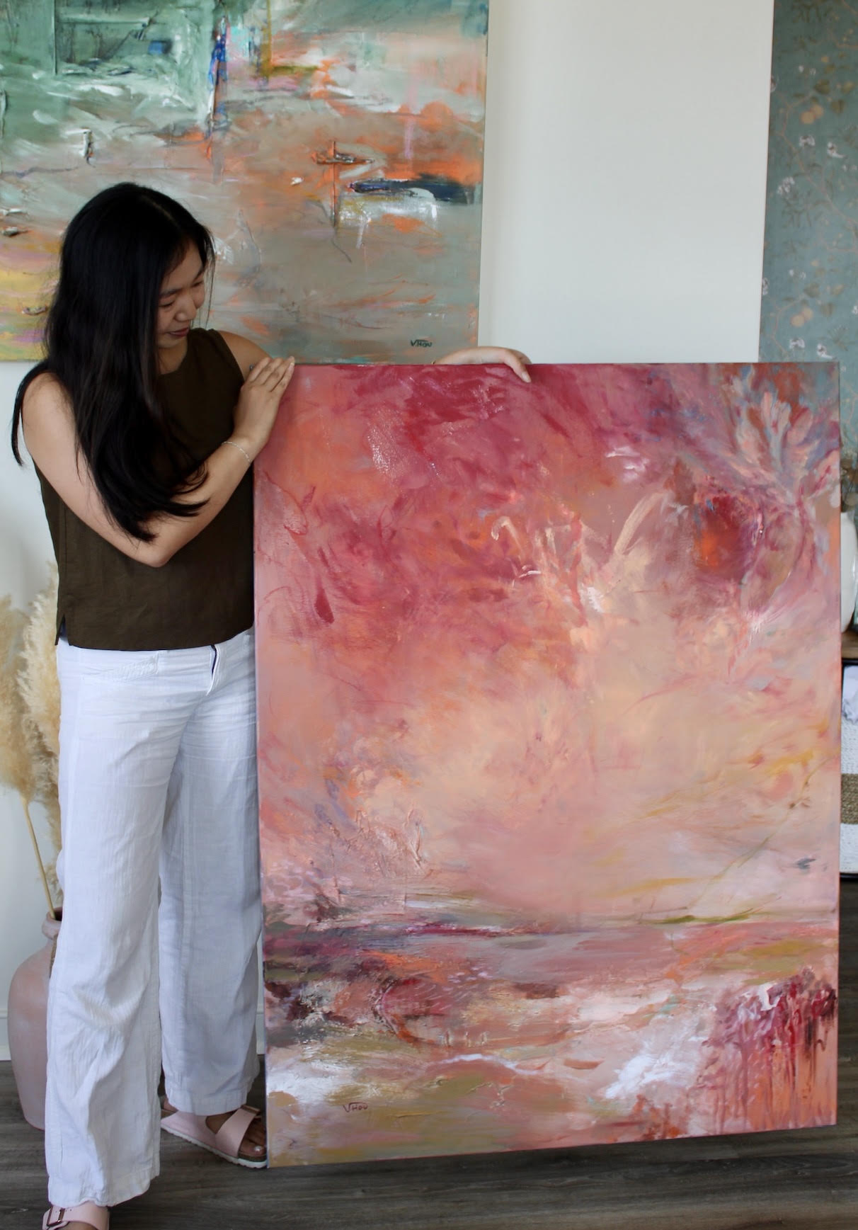 Woman with long dark hair holding a large abstract painting with pink, orange, and white colors.