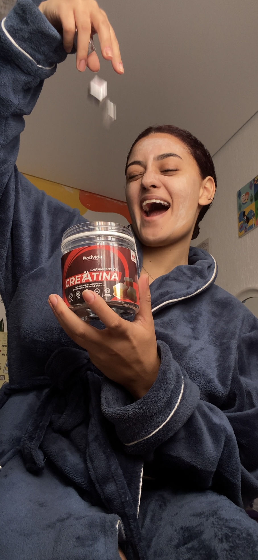 Young woman smiling and holding a container of creatine supplement, with a small white object in her hand.