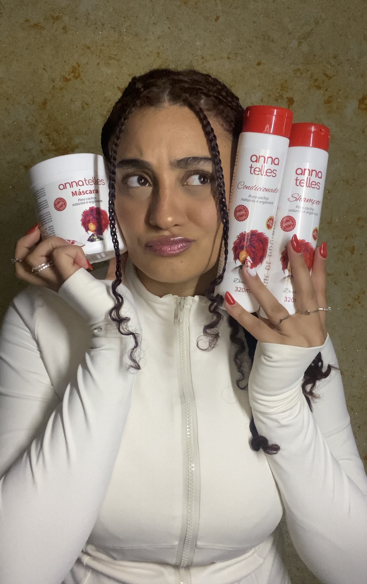 Woman holding three cans of raspberry-flavored beverage, looking at camera, wearing a white jacket, against a textured yellow background.