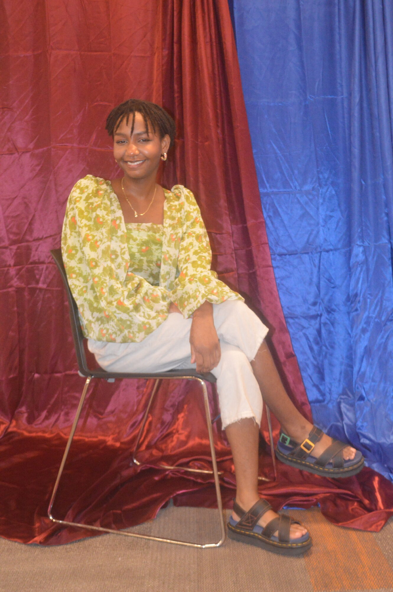 Woman sitting on a chair, smiling, with colorful curtains in the background.