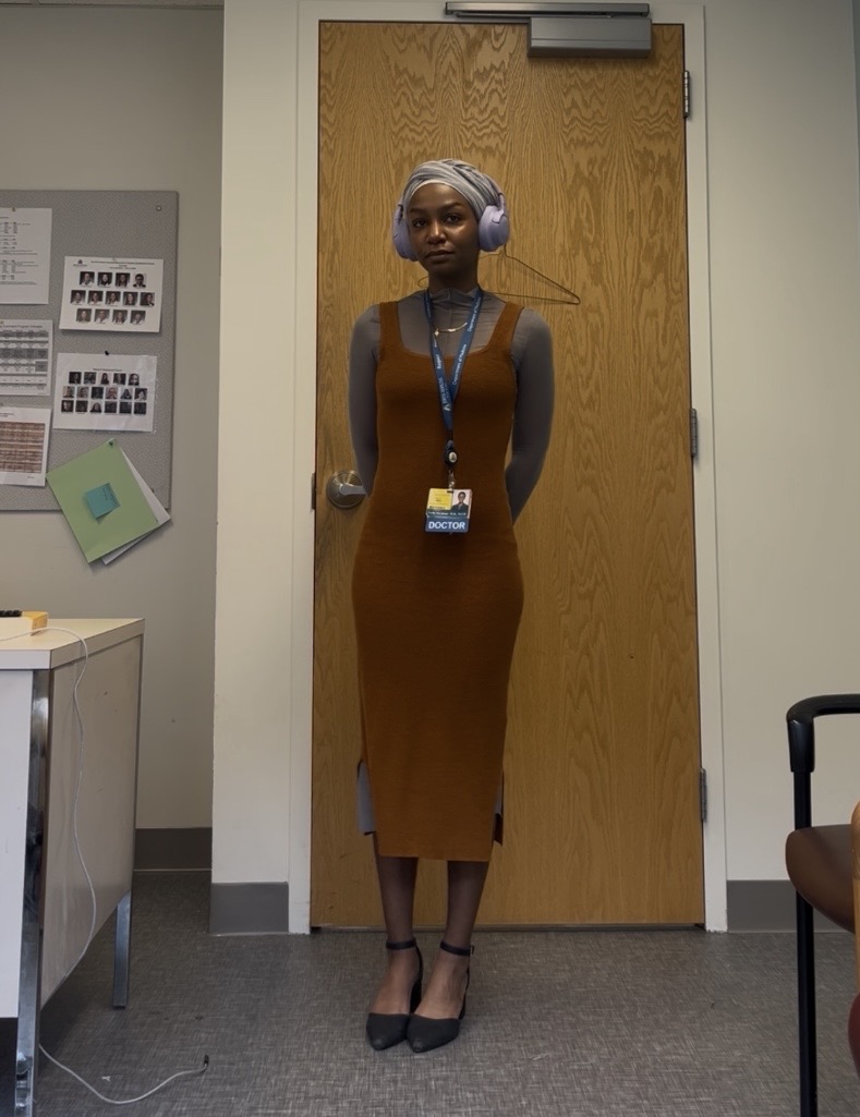 Woman with gray hair and headphones standing in front of a wooden door, wearing a long dress and heels.
