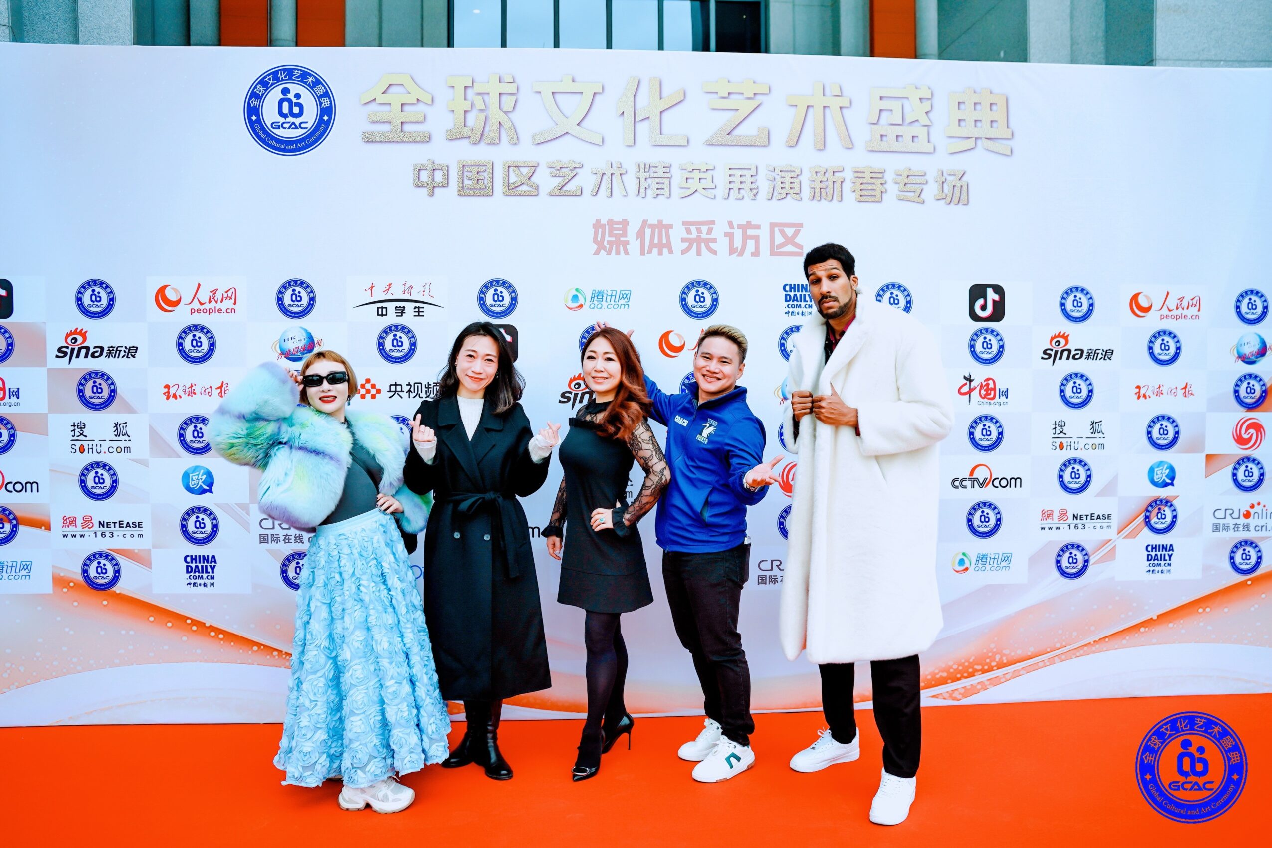 Five people standing on a red carpet in front of a backdrop with Chinese text and logos, smiling and posing for the photo.