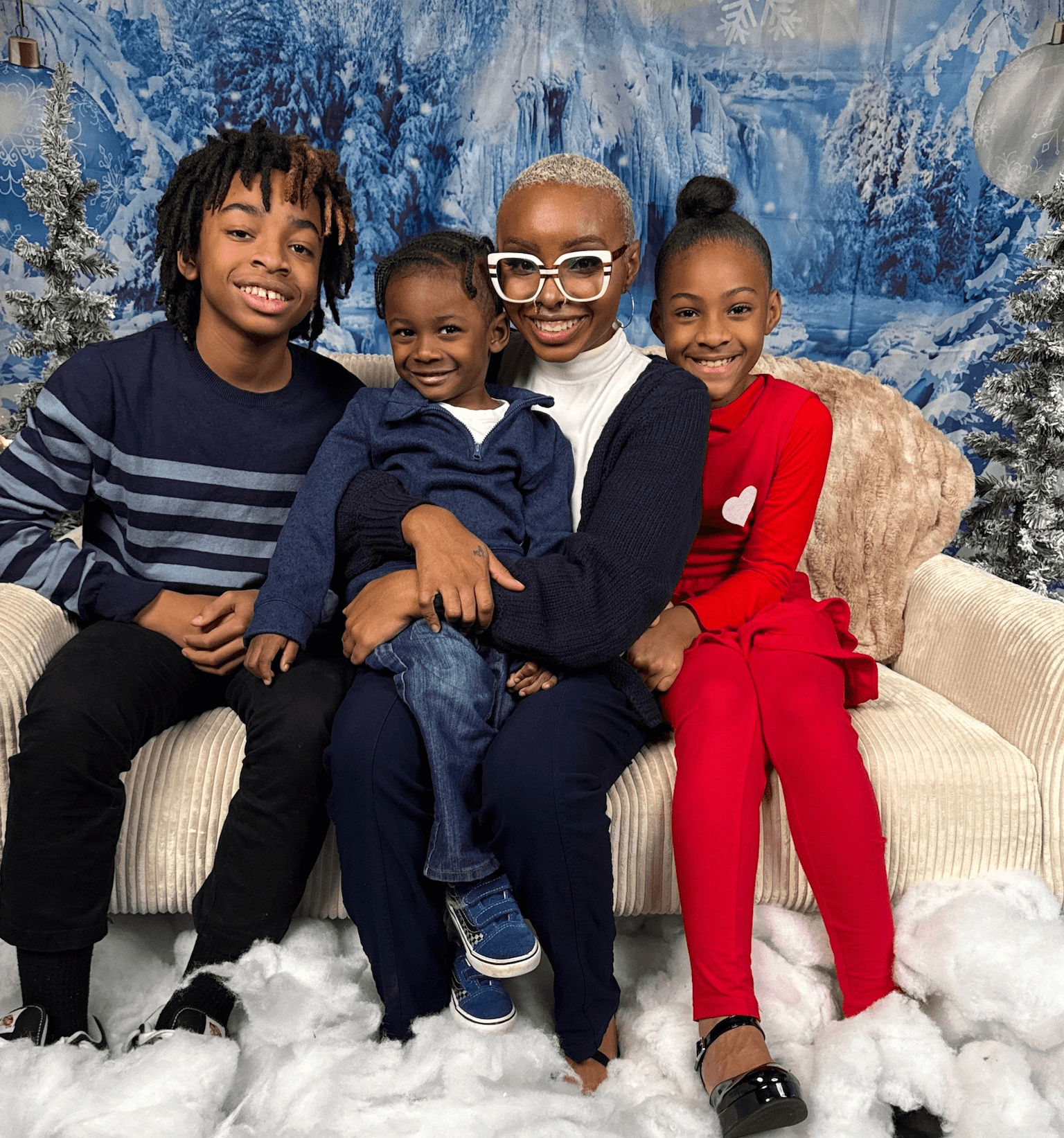 Four children sitting on a couch with a snowy winter backdrop, smiling and posing together.