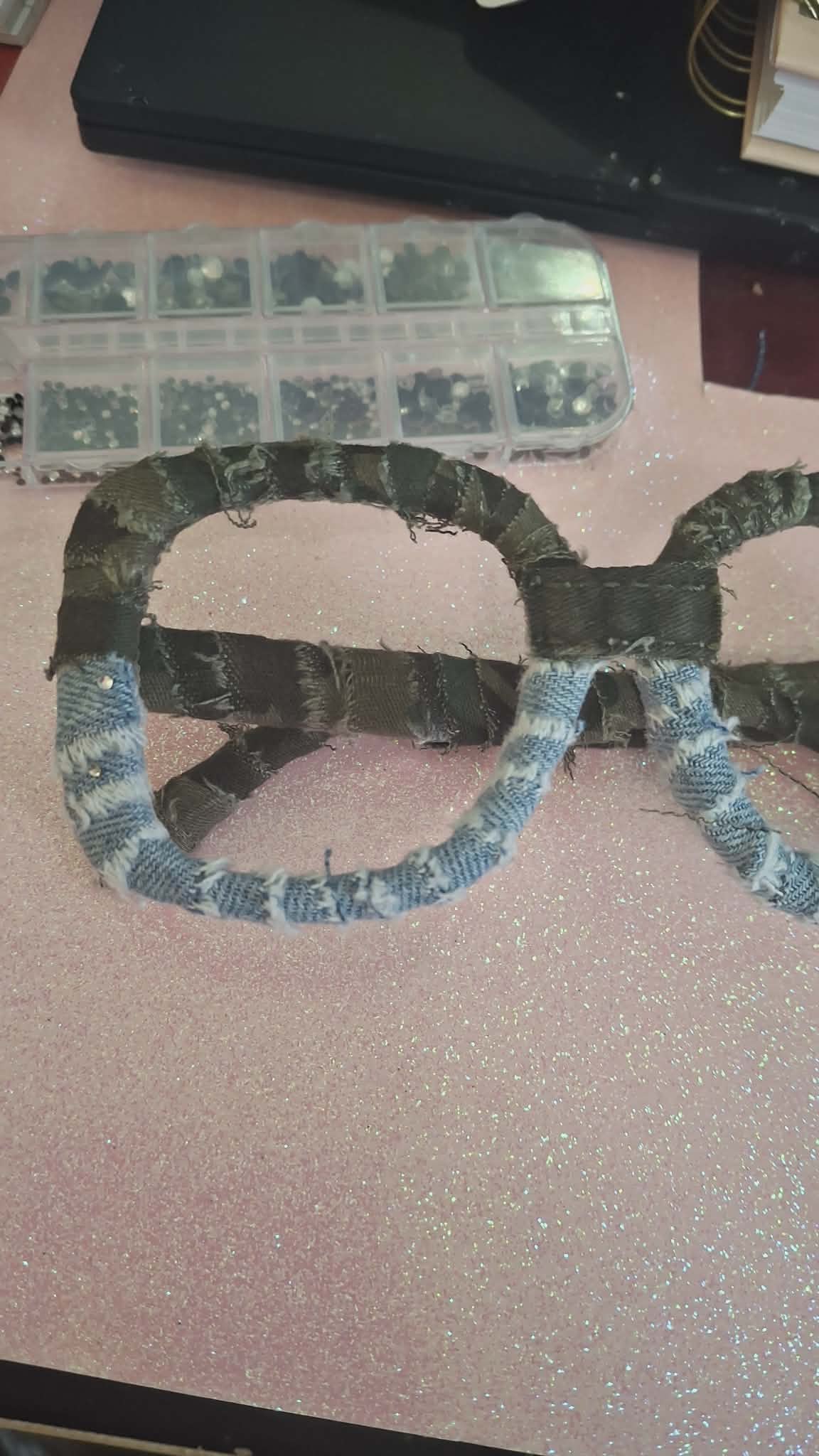 Colorful snake-shaped object made of fabric or paper, placed on a pink surface with a plastic container and books nearby.