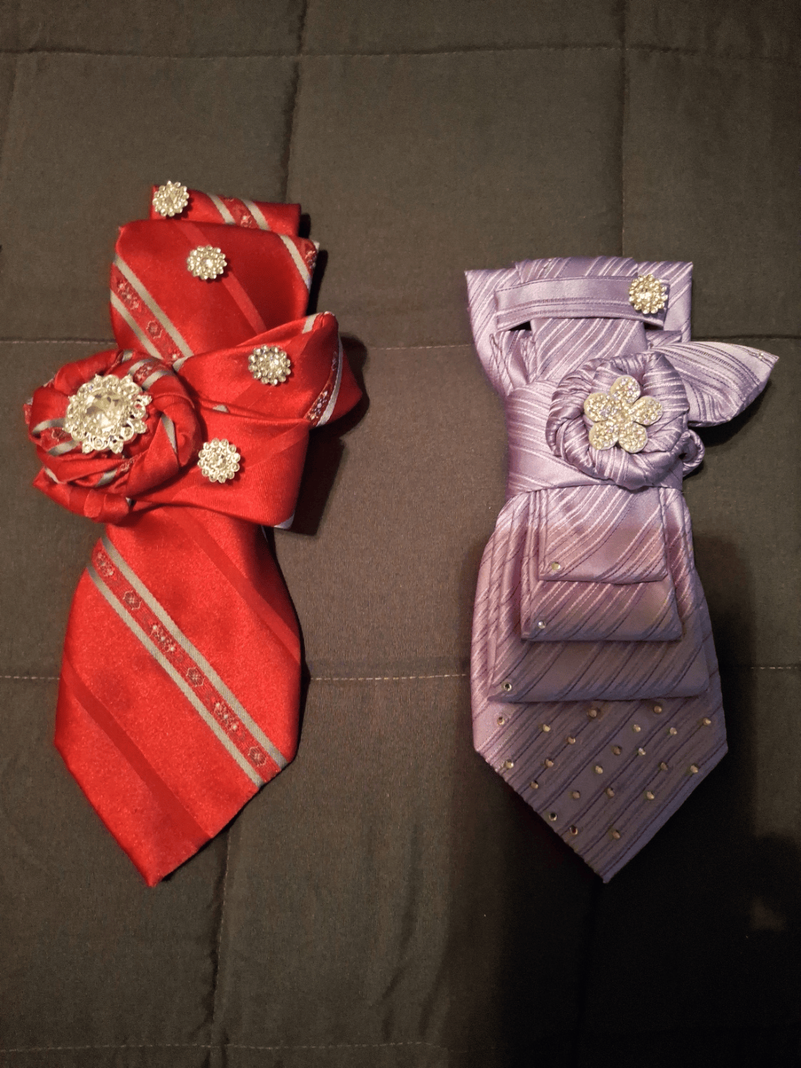 Two decorative bows, one red with floral embellishments and one purple with a flower, on a dark surface.