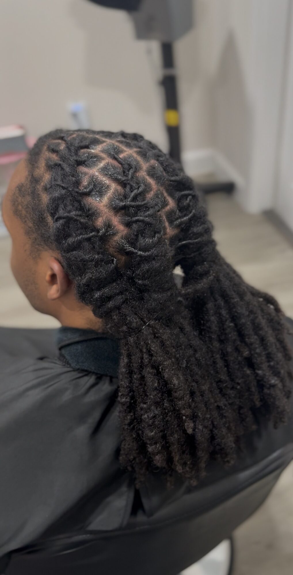 Person with styled dreadlocks sitting in a chair, facing away from the camera, indoors.