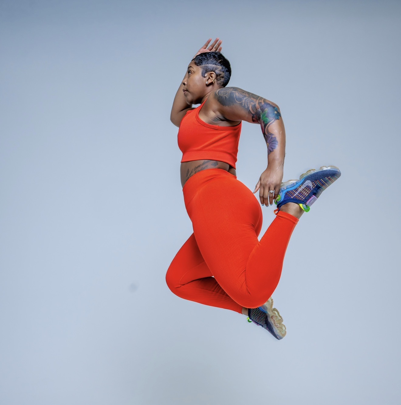 Person jumping with one hand on head, wearing red sportswear and colorful shoes, against a plain background.