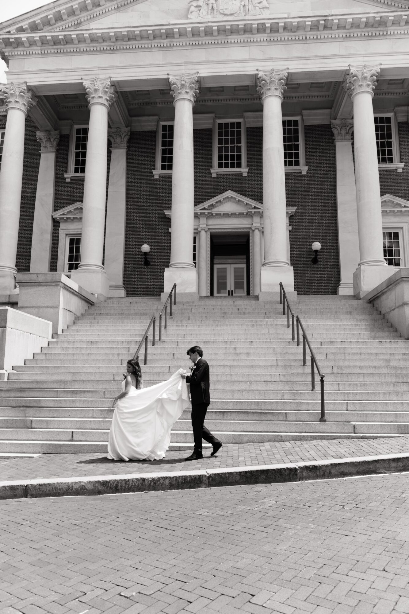 Couple dancing on stairs in front of a large building with columns, black and white photo.