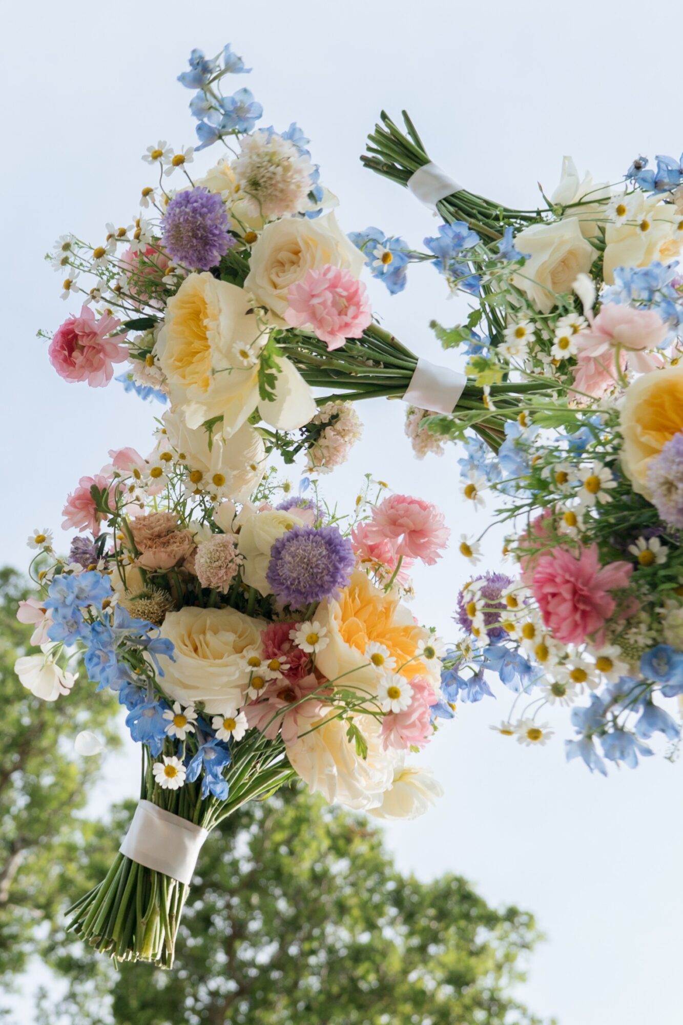 Bouquet of mixed flowers including roses, daisies, and other blooms against a light sky background.
