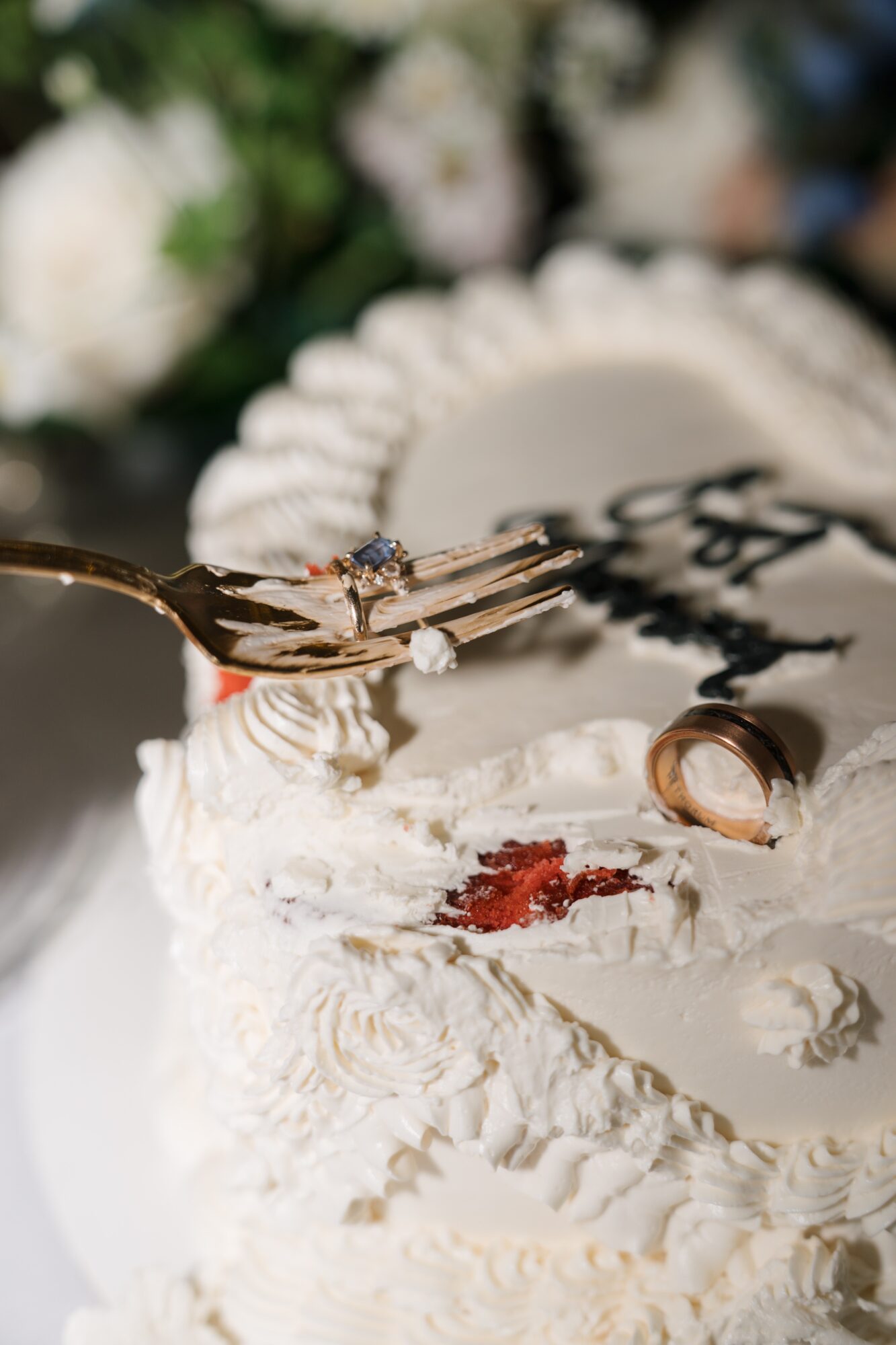 Cake with white frosting, a ring, and a fork with a piece of cake, blurred flowers in background
