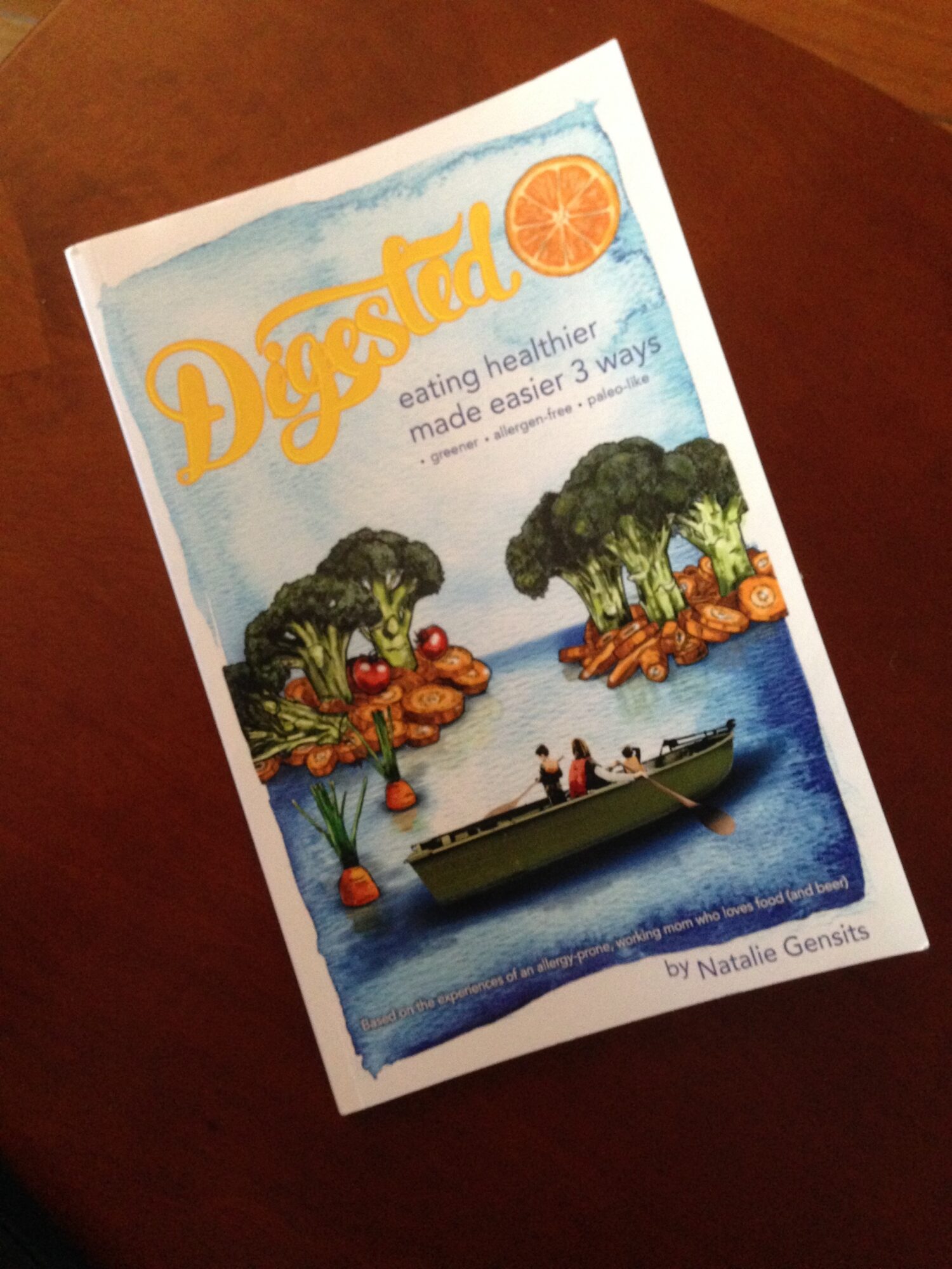Book cover titled 'Dandelion' with trees, a boat, and people on water, featuring a citrus slice and blue sky.