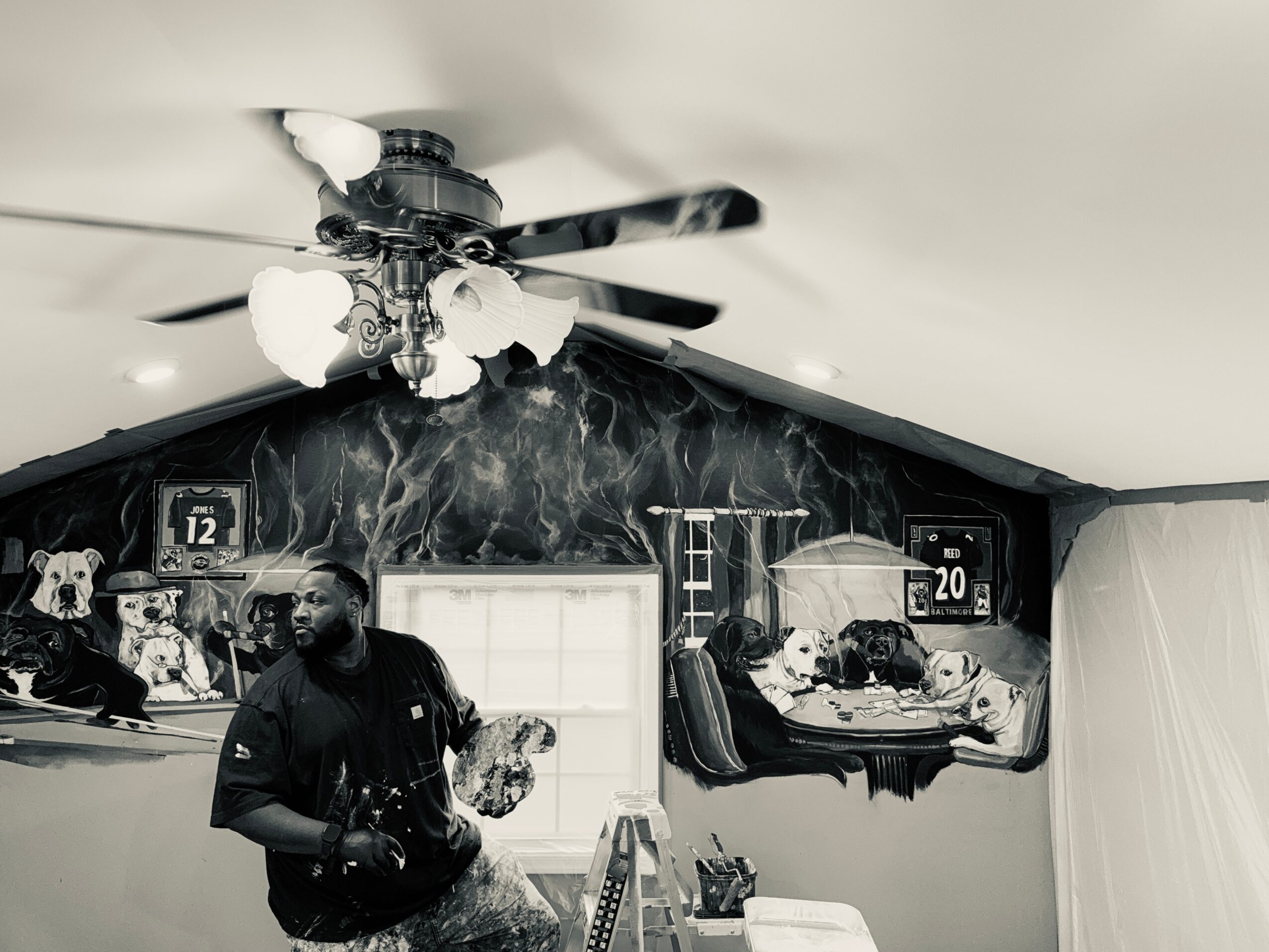Living room with a ceiling fan, a man holding a dog, and a window with a view outside, black and white photo.
