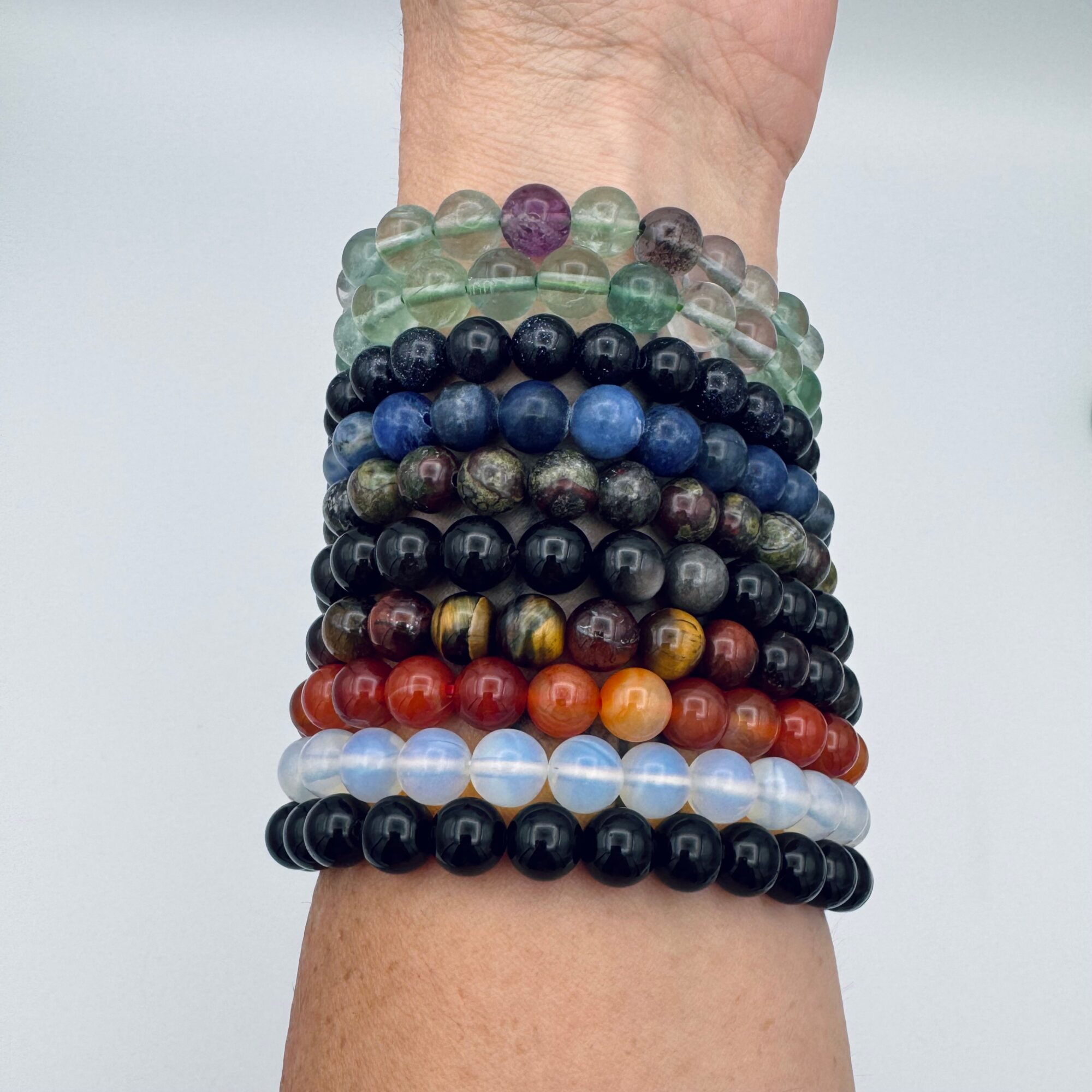 Multiple colorful beaded bracelets stacked on a person's wrist, with various colors and sizes of beads.