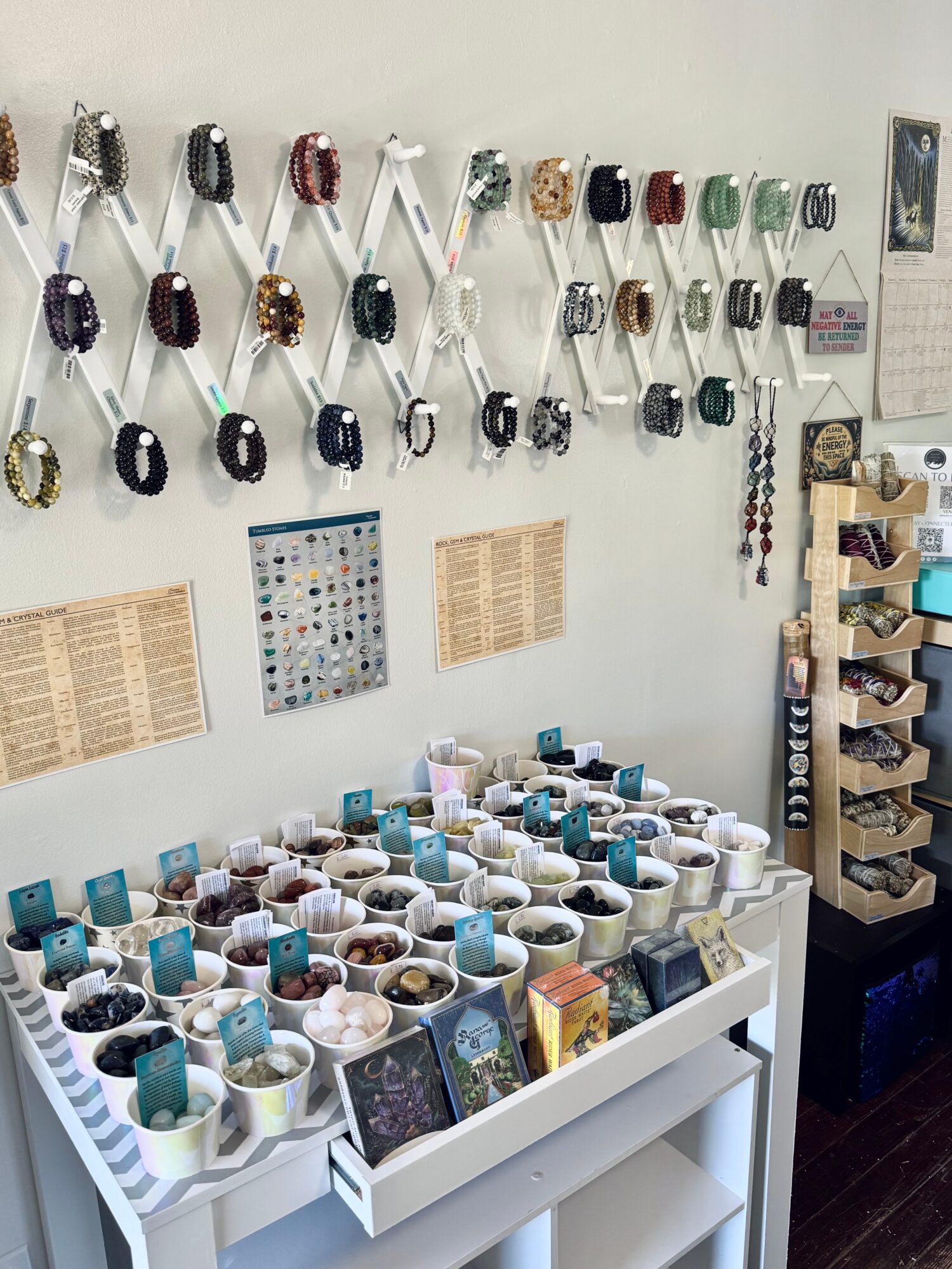 Display of jewelry and ceramic bowls on a white table, with jewelry hanging on the wall behind, and a wooden shelf on the right.
