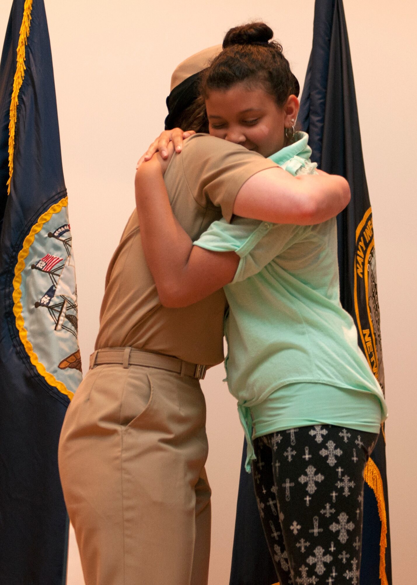 Two people hugging, one in a uniform and the other in casual clothing, with flags in the background.
