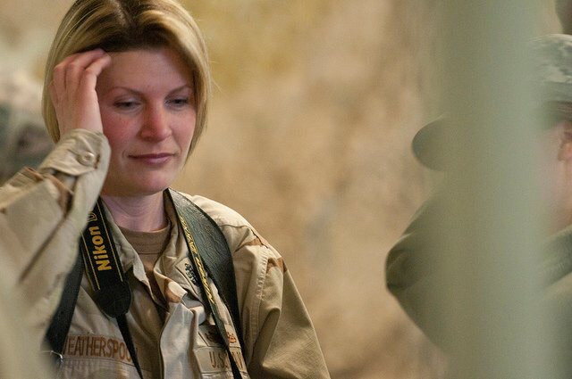 Woman with a Nikon camera around her neck, touching her hair, outdoors, neutral background