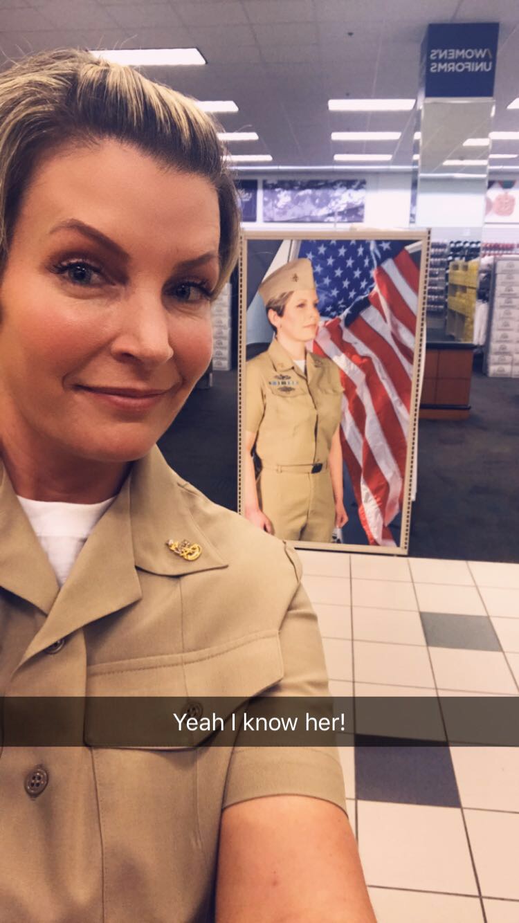 Woman taking a selfie in a store with a patriotic display and a mannequin in uniform behind her.