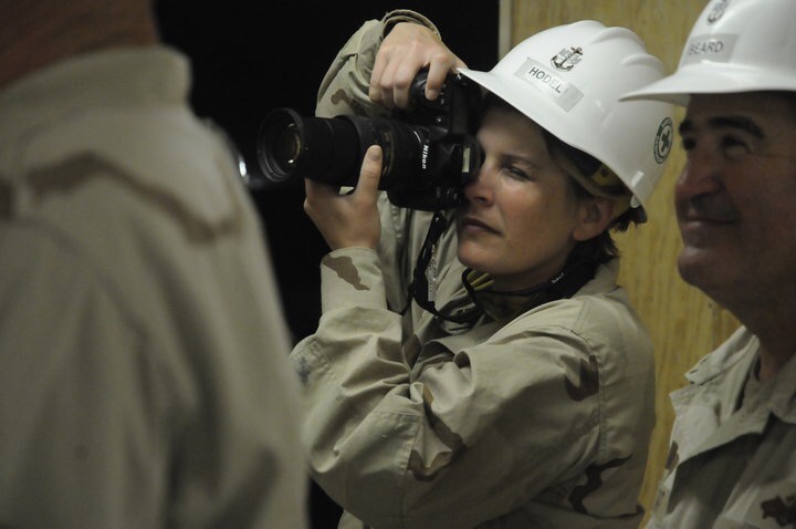 Group of people wearing safety helmets, one woman using a camera to take a photo, indoor setting