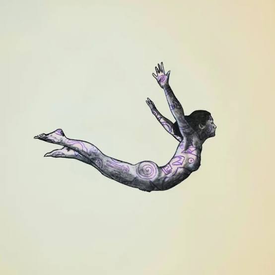 A person with tattoos is floating horizontally with arms and legs extended, against a plain light background.