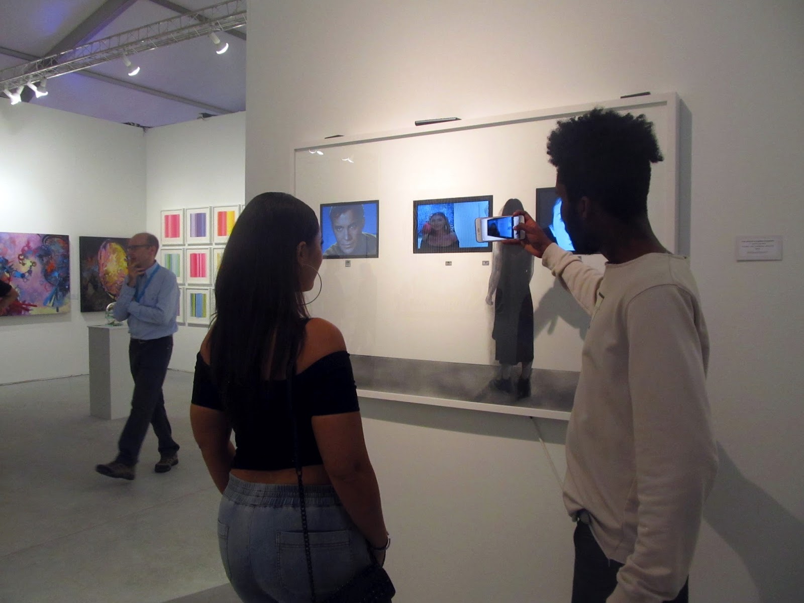 People in an art gallery, some taking photos of digital screens on the wall.